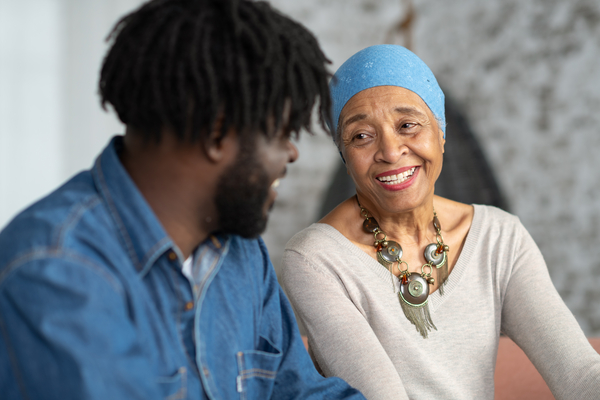 An African woman with cancer is happily spending time with her adult son in a living room. They are laughing and being affectionate.