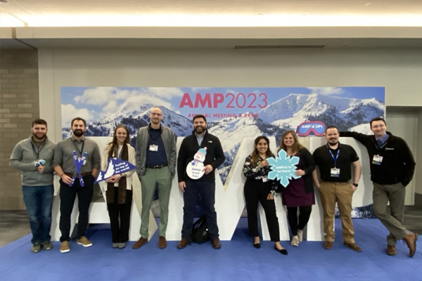 Our team standing in front of the AMP 2023 photo op space