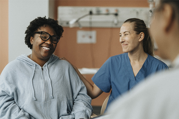 Provider and patient sitting in an exam room. The provider has her hand on the shoulder of the patient.